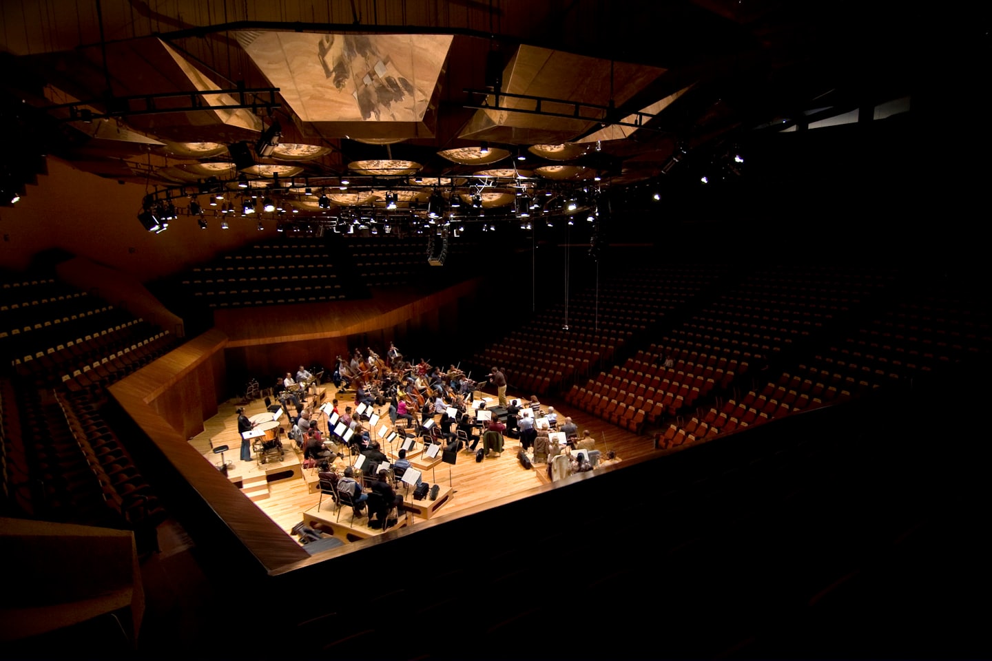 Orchesterprobe auf einer hell erleuchteten Bühne in einem modernen Konzertsaal.