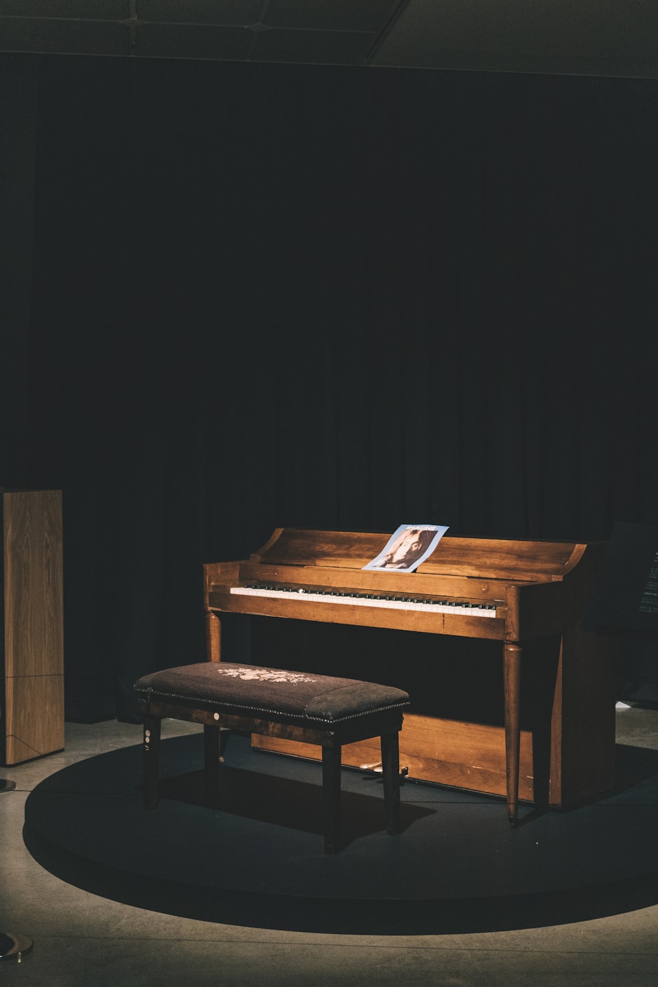 Ein hölzernes Klavier mit Klavierbank auf einer runden Bühne.
